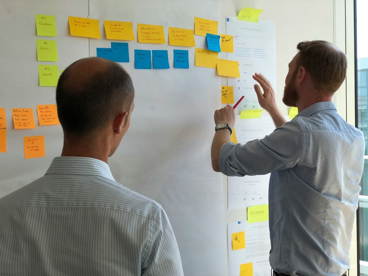 Two people working through a plan on a wall of sticky notes