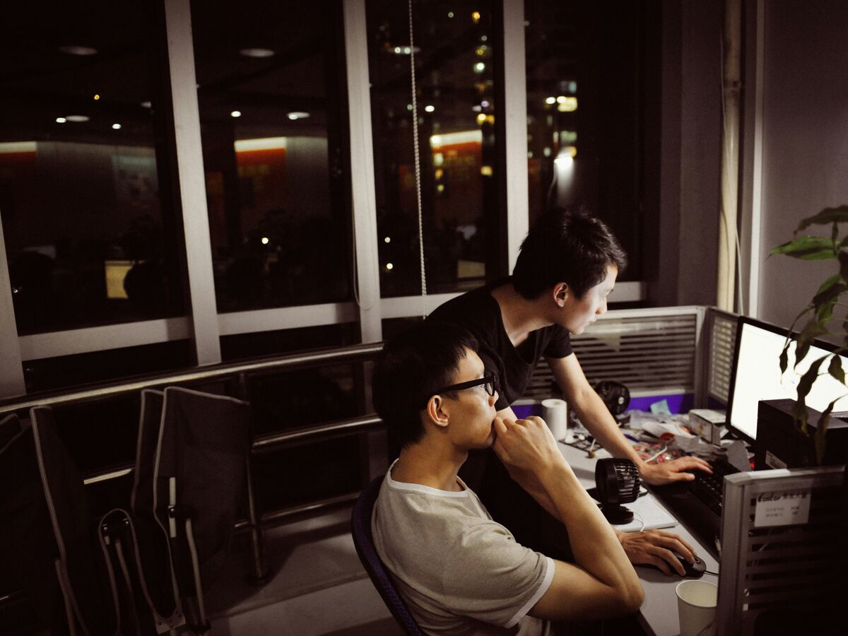 Two analysts studying a monitor in an office at night, city lights behind them