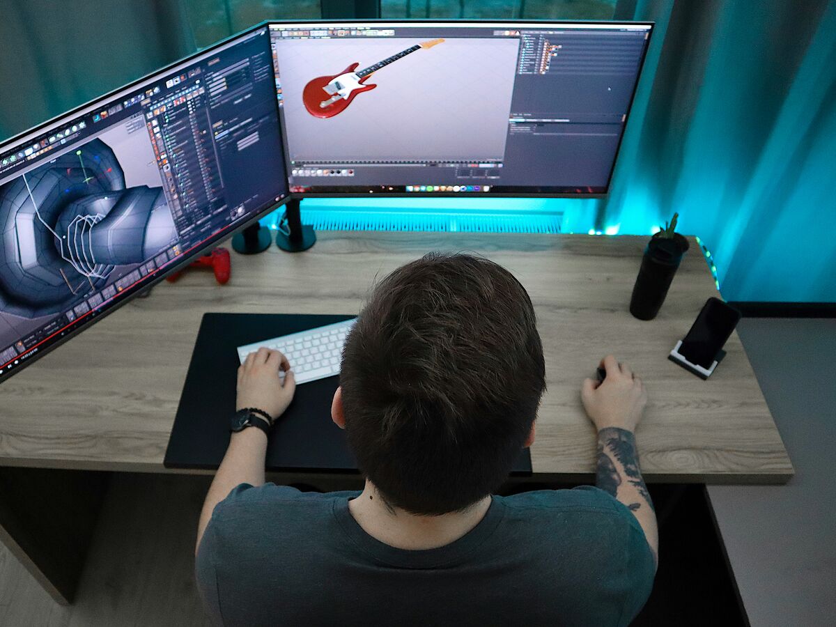 Engineer at a dual-monitor workstation rotating a CAD model of a mechanical assembly